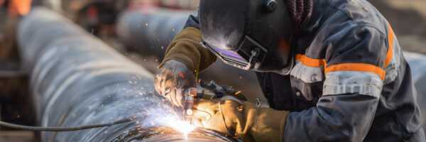 Soudage de pipelines sur un chantier industriel en plein air par un ouvrier en combinaison de protection.